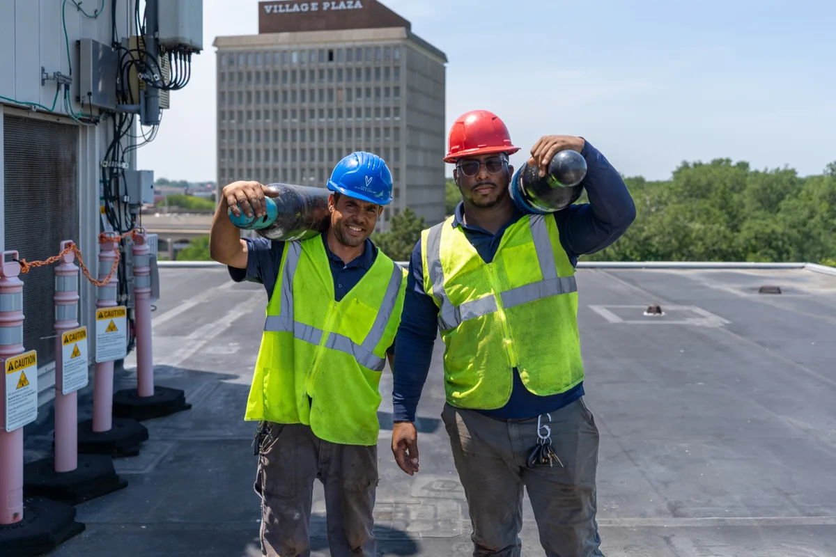 Two Vitality Mechanical technicians carrying cylinders on a rooftop